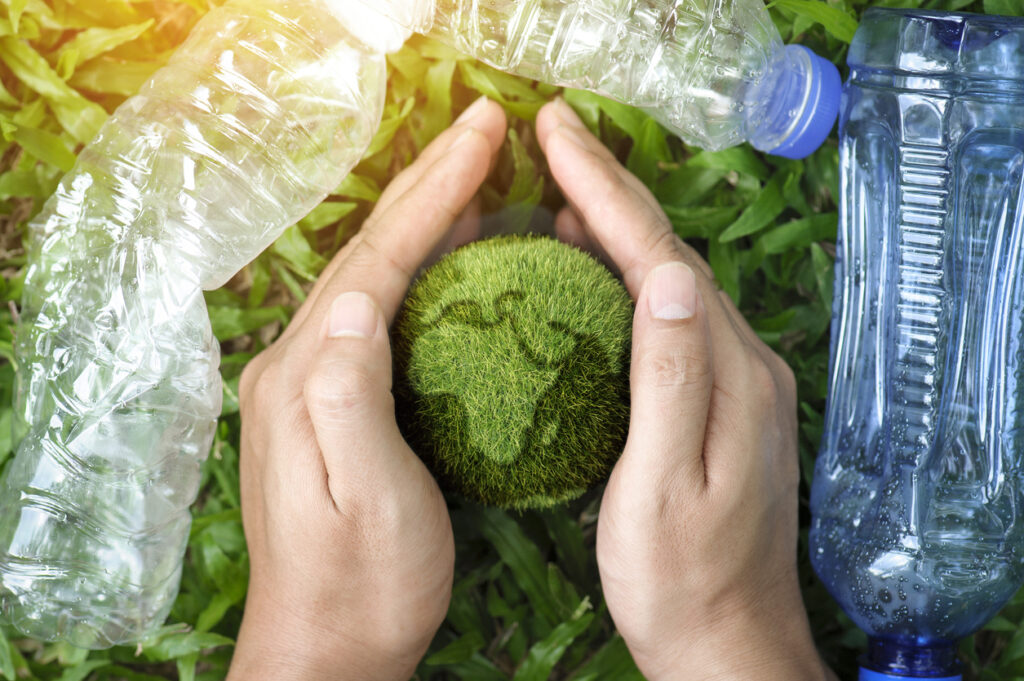 Hands holding and protecting the earth from plastic bottles